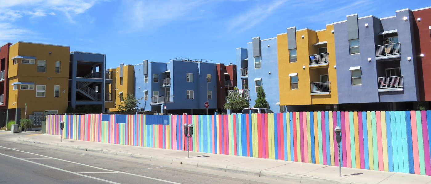 Colorful multistory apartment buildings behind a rainbow-painted fence under a clear blue sky, representing affordable neighborhoods in Albuquerque, NM.