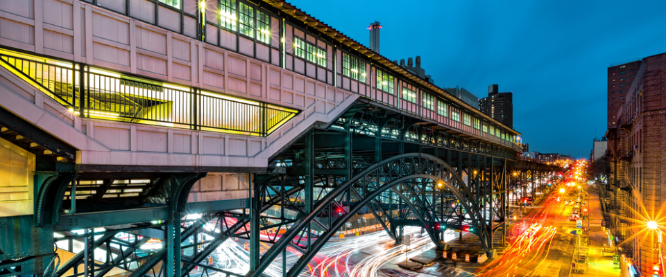 Elevated Metro-North train station lit up at dusk above a busy street with light trails from passing traffic, representing the Metro-North Harlem Line as part of public transit in White Plains, NY.