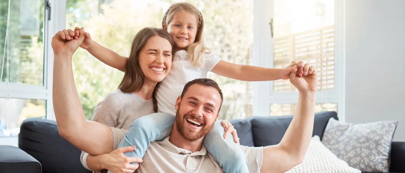 Smiling millennial parents and their young daughter relaxing together on a sofa, illustrating family life and the lifestyle of millennial renters with kids.