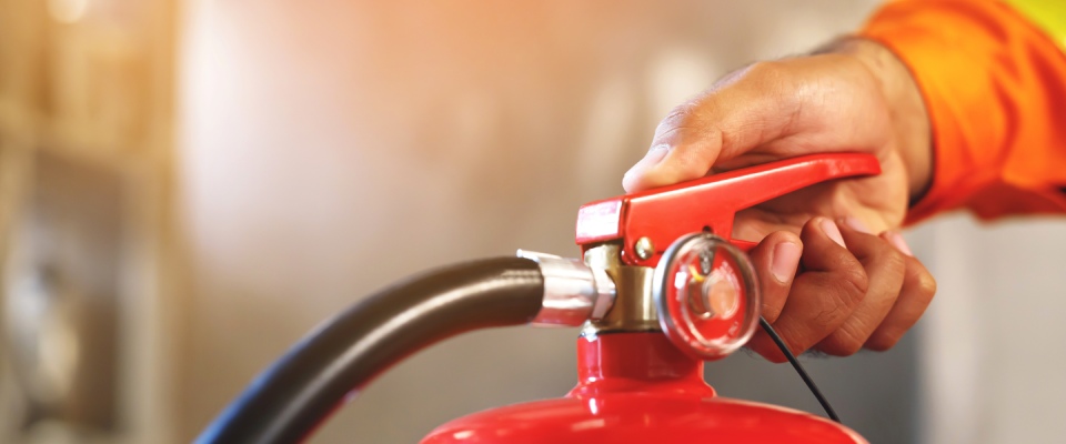 Hand operating a fire extinguisher during an emergency, highlighting building safety features and resident protection in apartments in Santa Barbara.