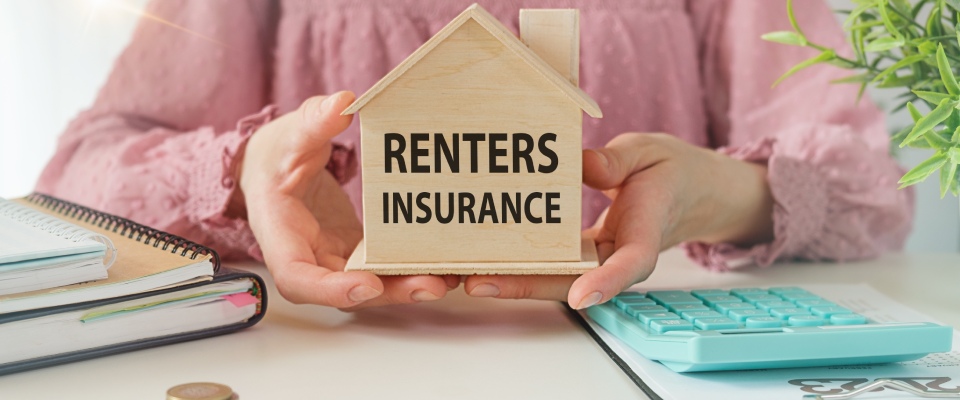 Woman holding a wooden house model with renters insurance messaging, highlighting financial protection and housing considerations for residents of apartments in McAllen.