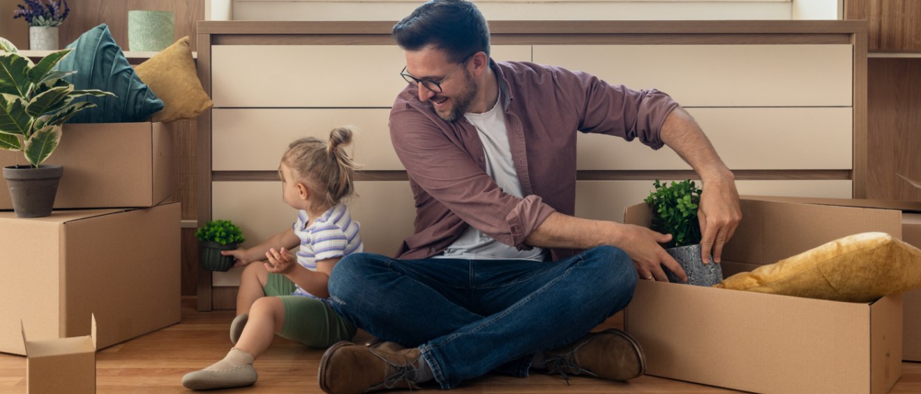 Single father and his young daughter unpacking moving boxes together in their new apartment after renting in a hot rental market.