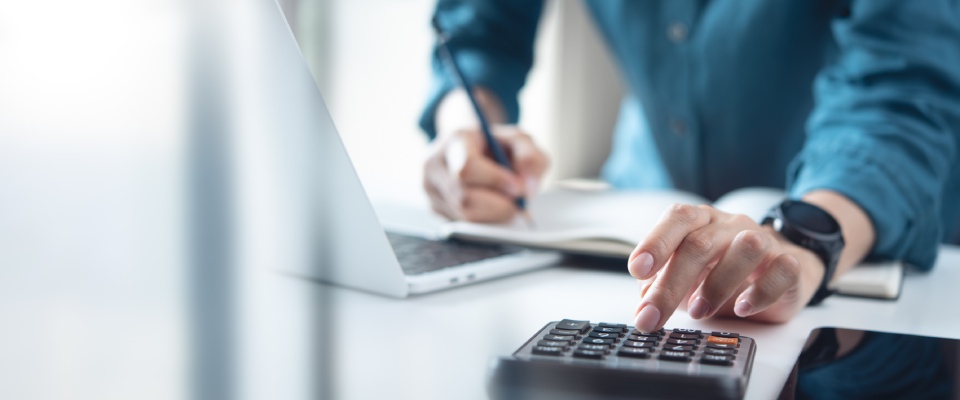 Person using a calculator and laptop to manage household finances, illustrating budgeting and financial planning for solo apartment life.