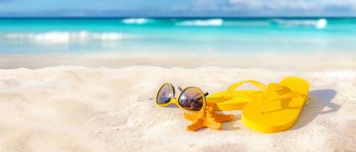 Sunglasses, a starfish, and yellow flip-flops resting on a sandy tropical beach under a bright blue sky on a sunny day, perfect for end-of-summer specials.
