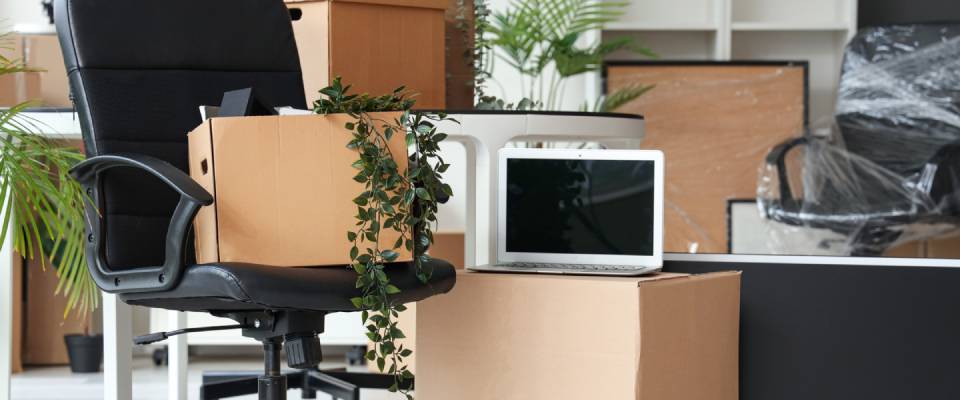 Interior of a modern office with a chair, laptop, and cardboard boxes on moving day featuring end-of-summer specials.
