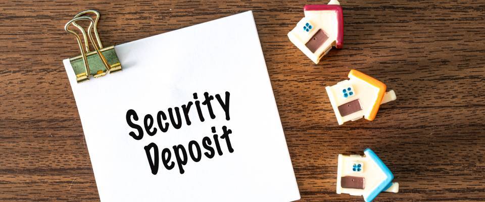 Security deposit text on white paper with toy houses and binder clips on a wooden desk representing a real estate rental concept for end-of-summer specials.