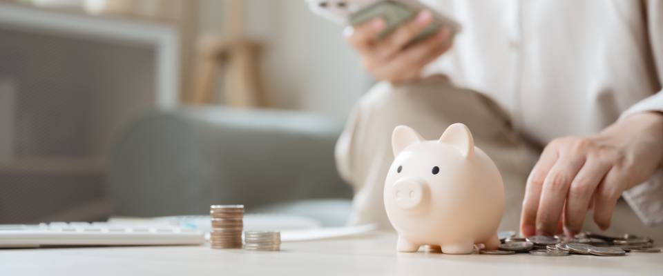 Piggy bank with coins and a person using a smartphone representing refunds, pending payments, and financial processing for end-of-summer specials.