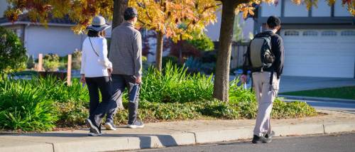 People walking on a pedestrian path with autumn leaves along the roadside in one of the walkable cities in California, USA.