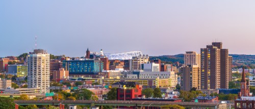 Syracuse, NY, downtown skyline at twilight with high-rise apartment towers and the university's domed stadium.