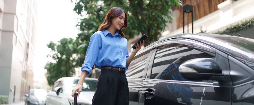 A business traveler stands on a city street with luggage, using a smartphone to hail a ride, showcasing the variety of public transit and transportation options available for daily commuters.