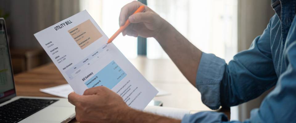 Man reviewing a utility bill with a pen at a home office desk representing household expenses, family budget, and financial management for apartments in Palo Alto.