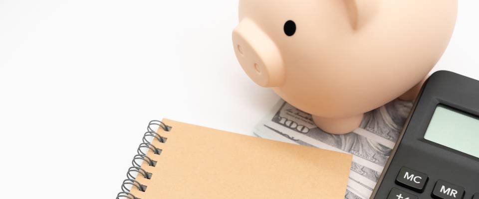 A piggy bank, notebook, and calculator arranged on a white background, representing the financial planning and budgeting considerations involved in how to break a lease.
